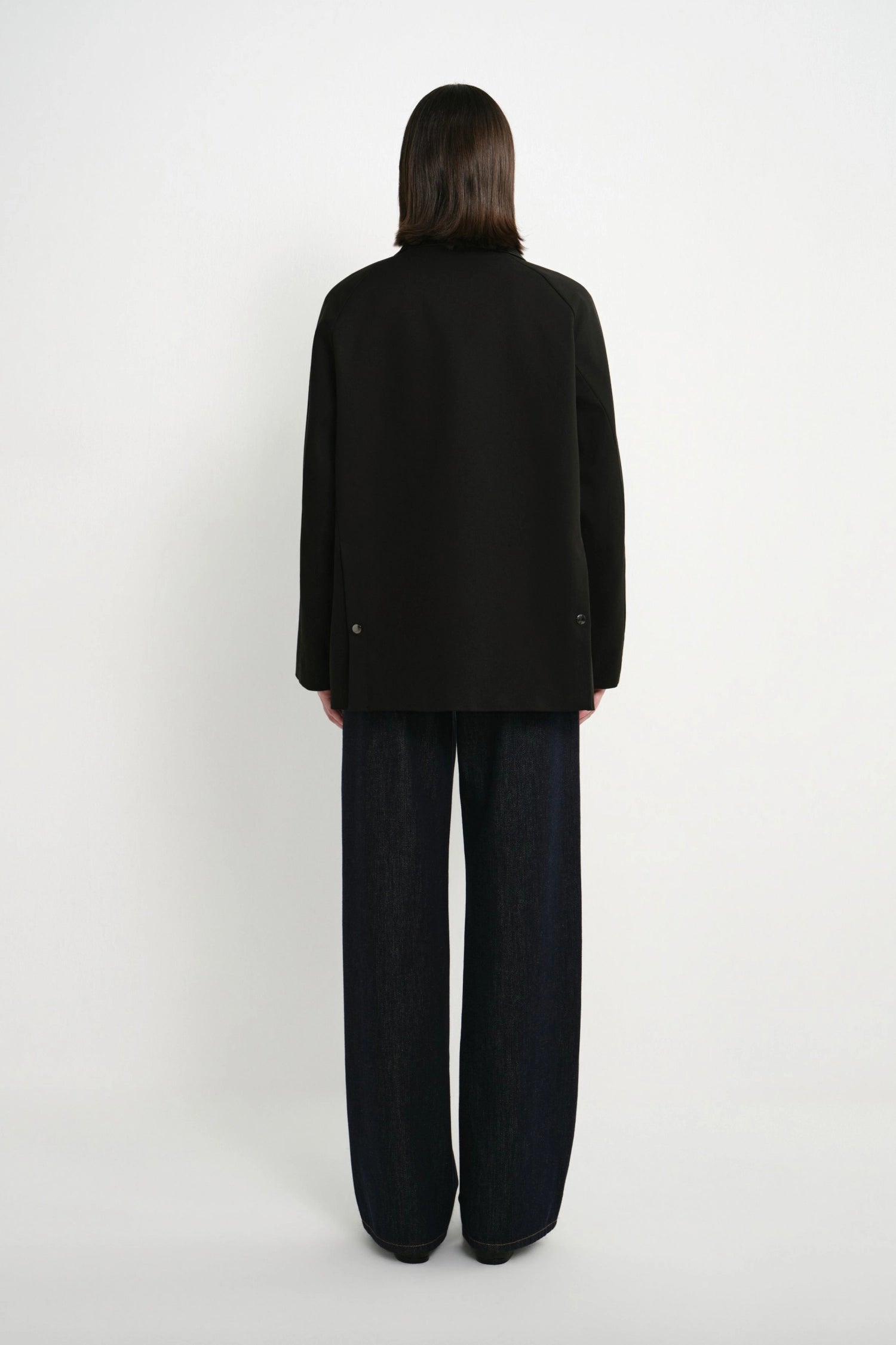 A model shown from the back wearing a black long-sleeve blazer and dark wide-leg trousers against a plain white studio background.