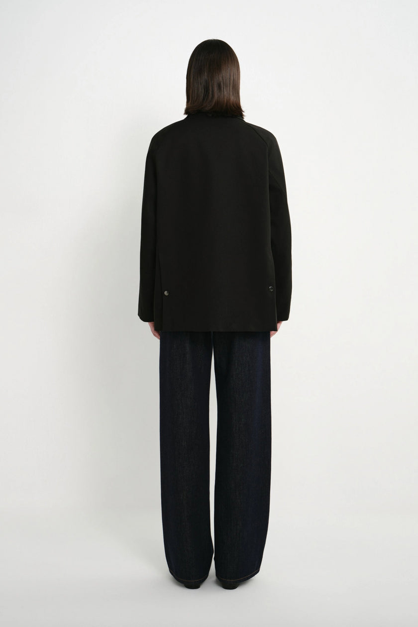 A model shown from the back wearing a black long-sleeve blazer and dark wide-leg trousers against a plain white studio background.