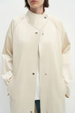 Close-up of the Rue Sophie Anne Satin Coat in crème, highlighting the high stand collar, metallic snap closures, raglan seam construction, side pockets, and smooth satin finish.