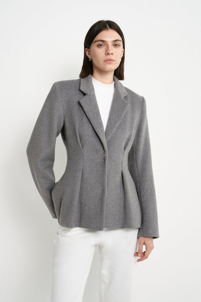 A model wearing the Rue Sophie Trenton Pleat Waist Wool Blazer in charcoal, highlighting the notched lapels, defined waist shaping, and structured tailored silhouette.