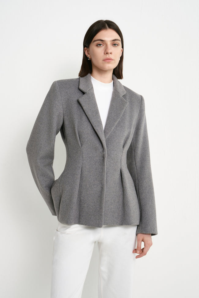 A model wearing the Rue Sophie Trenton Pleat Waist Wool Blazer in charcoal, highlighting the notched lapels, defined waist shaping, and structured tailored silhouette.