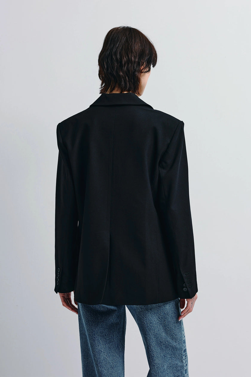 Back view of a woman wearing the Walker Oversized Black Blazer with denim jeans, showing tailoring details.