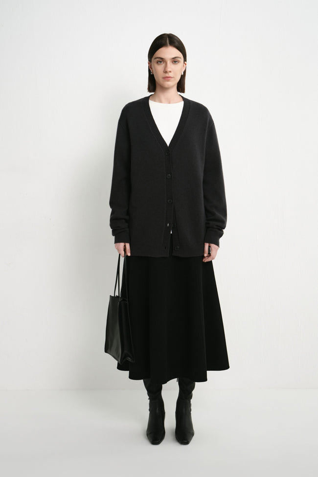 A model wearing the Rue Sophie Siho Cardigan Sweater in charcoal, featuring a deep V-neckline, button-front closure, long sleeves, and a relaxed oversized silhouette, full-length front view.