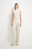 A model wearing a Rue Sophie creme sleeveless mock-neck top with a softly draped high neckline and clean straight silhouette, front view.