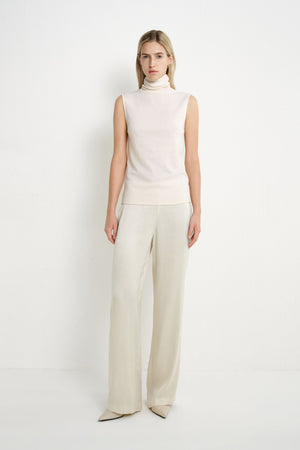 A model wearing a Rue Sophie creme sleeveless mock-neck top with a softly draped high neckline and clean straight silhouette, front view.