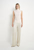 A model wearing a Rue Sophie creme sleeveless mock-neck top with a softly draped high neckline and clean straight silhouette, front view.