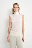 A model wearing a Rue Sophie creme sleeveless mock-neck top with a softly draped high neckline and clean shoulder construction, front view.