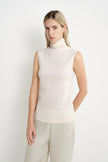 A model wearing a Rue Sophie creme sleeveless mock-neck top with a draped high neckline and subtle textured finish, three-quarter front view.