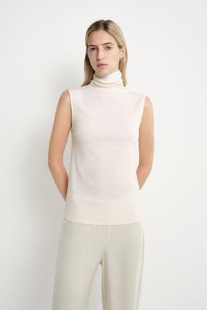 A model wearing a Rue Sophie creme sleeveless mock-neck top with extended shoulders, a softly draped neckline, and relaxed straight fit, full-length front view.