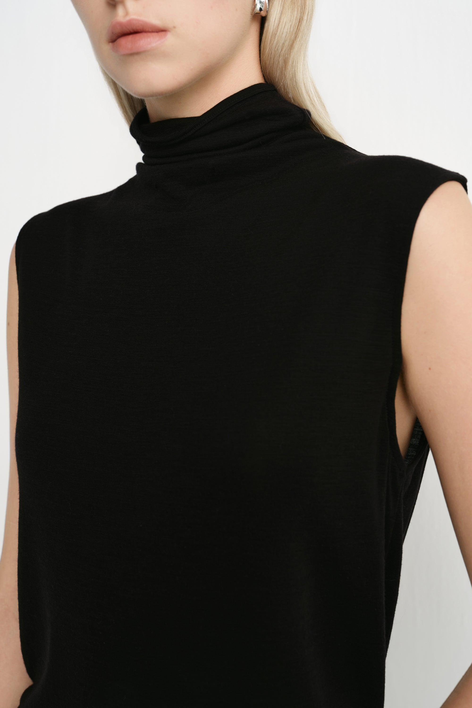 Close-up of a Rue Sophie black sleeveless mock-neck top featuring a softly draped high neckline and clean shoulder construction.