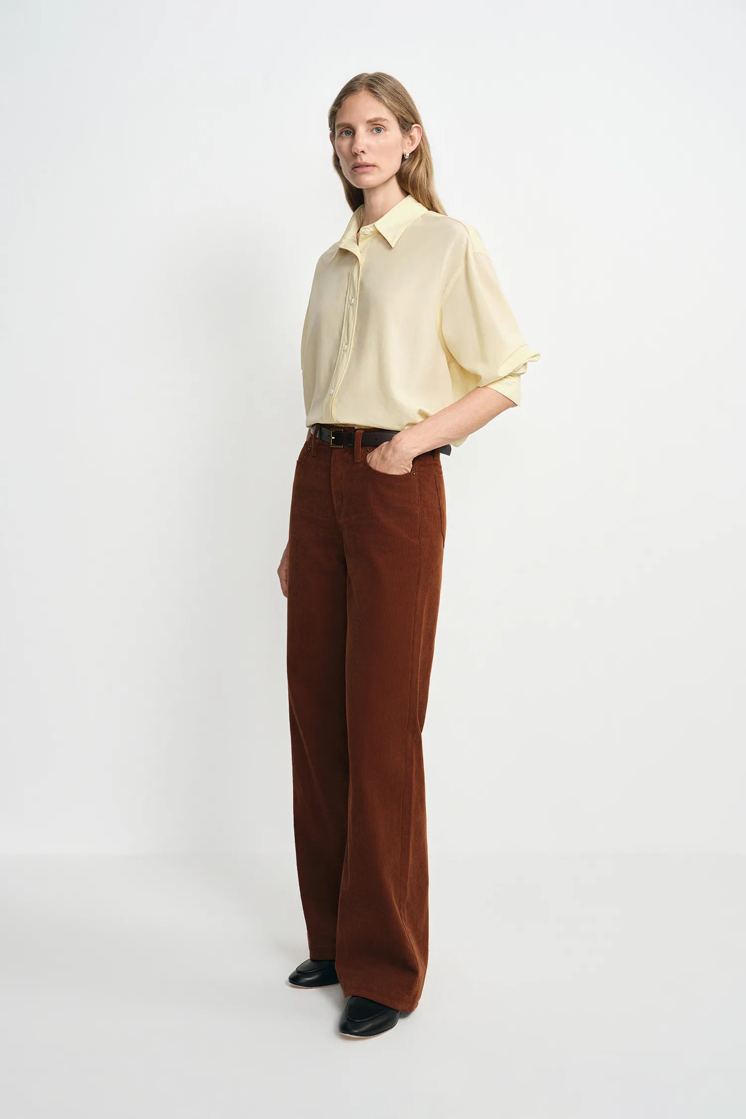 A model wearing a brown corduroy pant with a relaxed straight leg, side view.