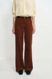 A model wearing high-waisted, wide-leg brown corduroy trousers with a dark brown belt, paired with a cream button-down shirt and black shoes, against a plain light gray background.