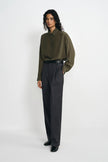 A model wearing dark grey pleat-front wide-leg trousers in a silky wool blend, pairing an olive shirt with a black belt and black loafers.