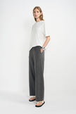 A woman modeling a white short-sleeve top and dark gray wide-leg trousers, standing against a plain white studio background.