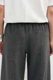 Close-up of a person wearing dark charcoal gray wide-leg trousers and a white top, cropped from the chest down against a plain light background.