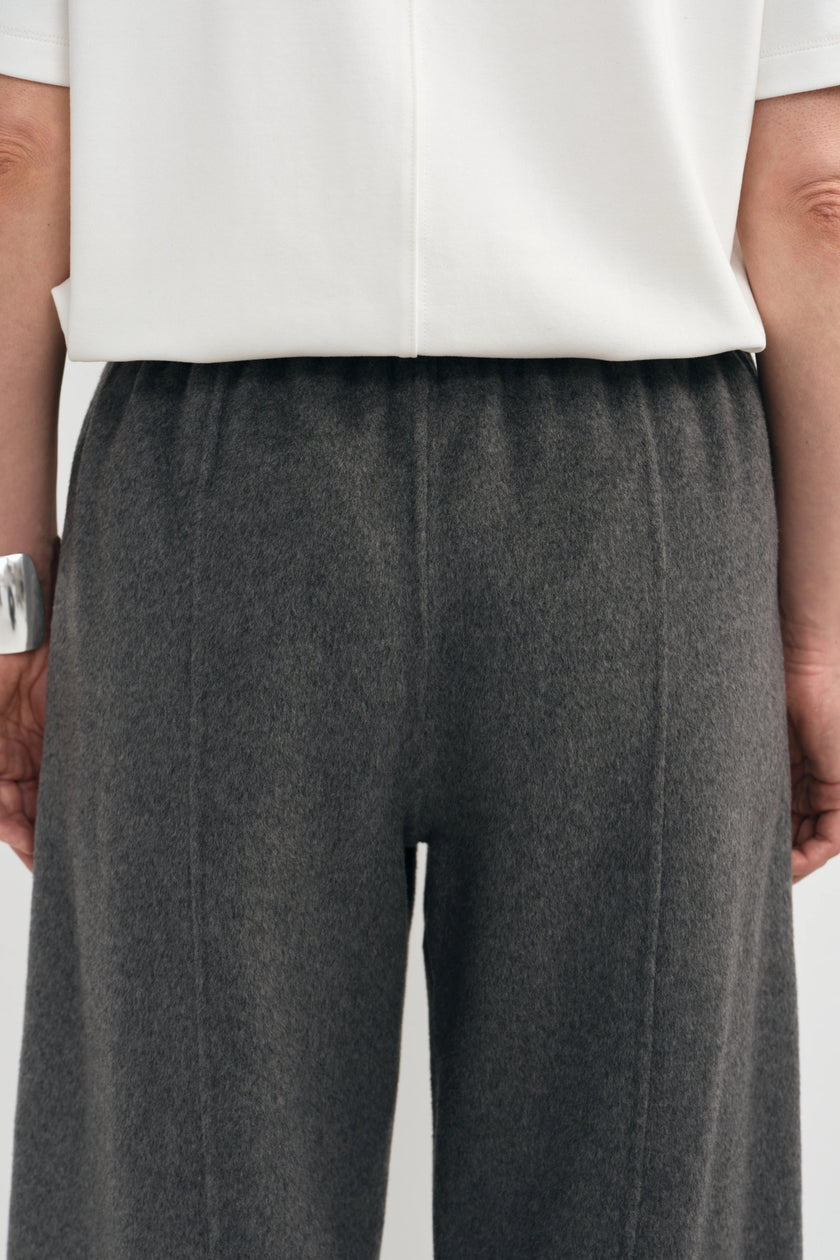 Close-up of a person wearing dark charcoal gray wide-leg trousers and a white top, cropped from the chest down against a plain light background.