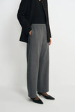 A model wearing a pair of wide-leg gray wool trousers, styled with a black blazer, black top, and black pointed-toe heels against a plain light gray studio background.
