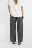 A model shown from the back wearing wide-leg gray trousers, a white short-sleeve top, and black flat shoes against a plain white studio background.