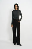 A model stands against a plain white studio background wearing a dark gray long-sleeve top and dark brown wide-leg trousers.