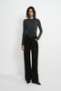 A model stands against a plain white studio background wearing a dark gray long-sleeve top and dark brown wide-leg trousers.
