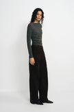 A woman modeling a dark gray long-sleeve top and dark brown wide-leg trousers against a plain white studio background.