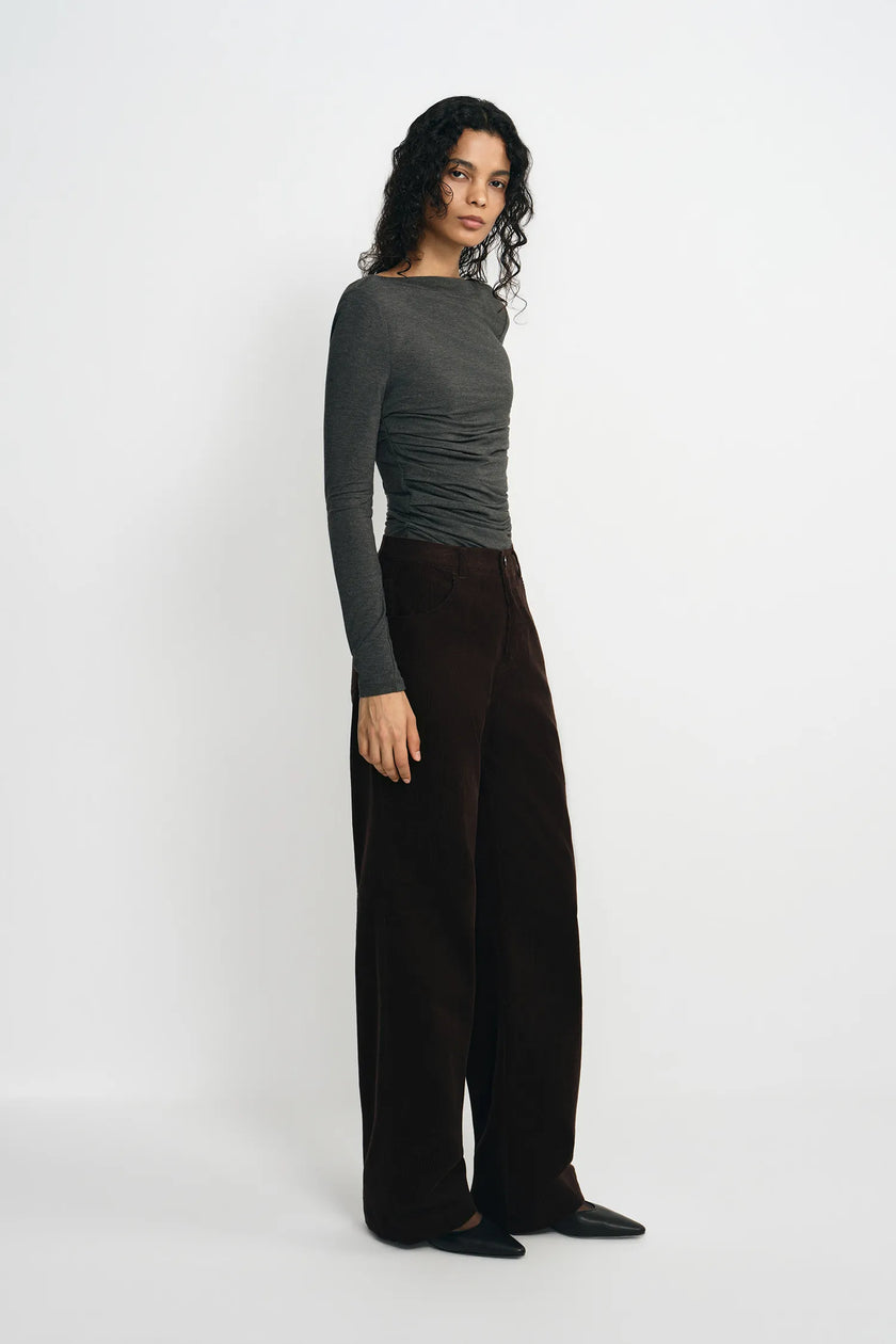 A woman modeling a dark gray long-sleeve top and dark brown wide-leg trousers against a plain white studio background.