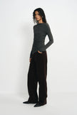 A model stands in profile wearing a dark charcoal gray long-sleeve ruched top and dark brown wide-leg trousers against a plain white studio background.