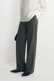 Close-up of charcoal trousers on a model, showing fine vertical stripes and straight legs extending over black pointed shoes beneath a white blouse.