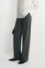 Close-up of charcoal trousers on a model, showing fine vertical stripes and straight legs extending over black pointed shoes beneath a white blouse.