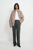 A model facing forward in charcoal pinstriped trousers with straight legs, paired with an open taupe jacket, white T-shirt and black pointed shoes.