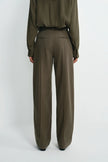 A model shown from the back wearing a matching olive green long-sleeve blouse and wide-leg trousers, photographed against a plain light gray studio background.