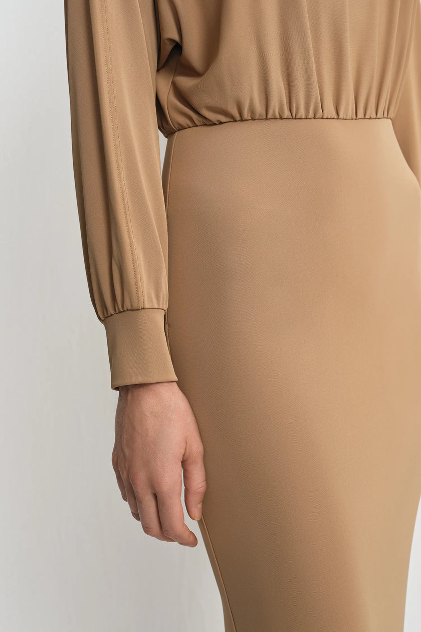 Close-up detail of a camel soft knit maxi dress, showing the gathered elastic waistband and ribbed cuff with fine knit texture.