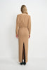 A model wearing a camel soft knit maxi dress with a fitted waist and rear slit detail, pairing black pointed-toe heels with sheer black tights.