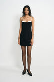 A model wearing a black mini dress with a white contrast panel at the neckline and thin straps.