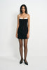 A model wearing a black mini dress with a white contrast panel at the neckline and thin straps.