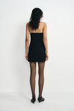 A model wearing a black mini dress with white straps, back view.