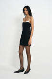 A model wearing a black mini dress with a white contrast panel at the neckline, turned slightly to the side.