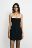 A model wearing a black mini dress with a white contrast panel at the neckline and thin straps, facing the camera.