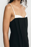 Close-up of a model wearing a black dress with a white sweetheart neckline and thin spaghetti straps against a light gray background.