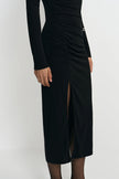 A black long-sleeve midi dress with ruching and a thigh-high slit, shown on a model against a plain light gray studio background.