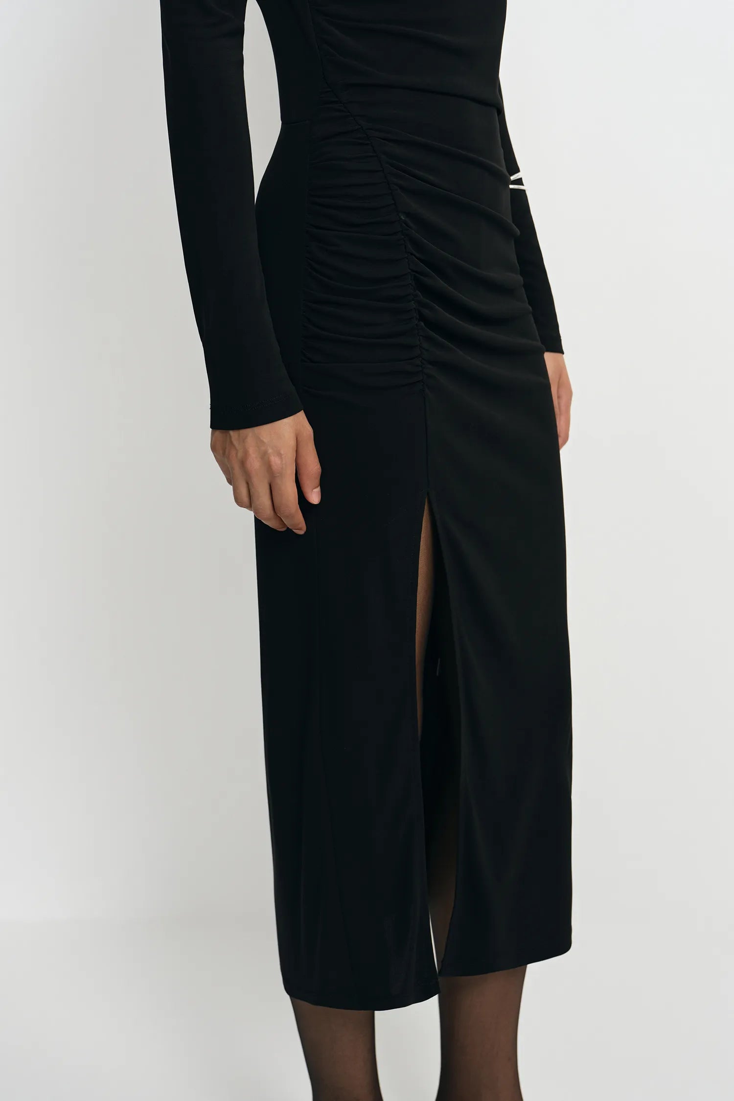 A black long-sleeve midi dress with ruching and a thigh-high slit, shown on a model against a plain light gray studio background.