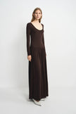 A woman modeling a dark brown long-sleeve maxi dress with a scoop neckline and a flowing skirt, standing against a light gray studio background.