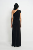 Back view of a model wearing a black maxi dress with a one-shoulder neckline and diagonal folds across the back above the long skirt.