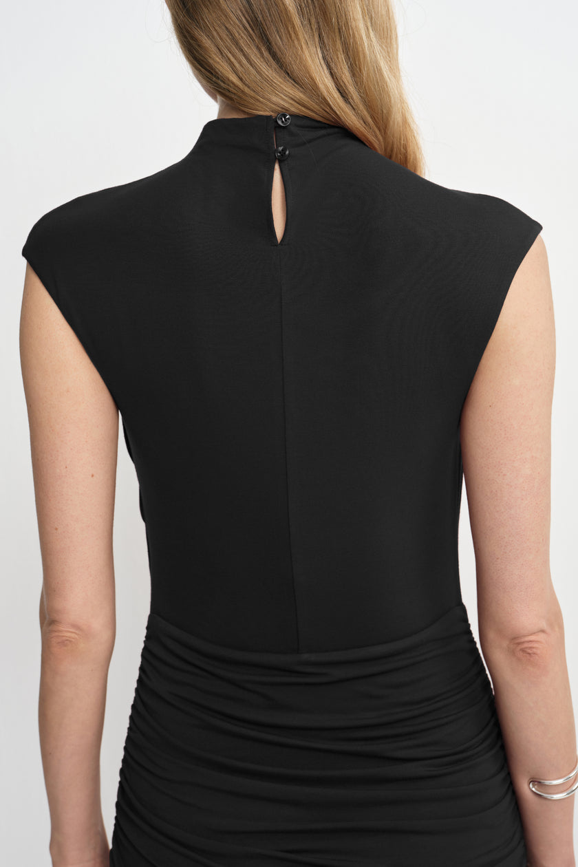 Close-up of a black dress from behind on a model, showing a buttoned keyhole at the high neckline, center-back seam and gathered waist.