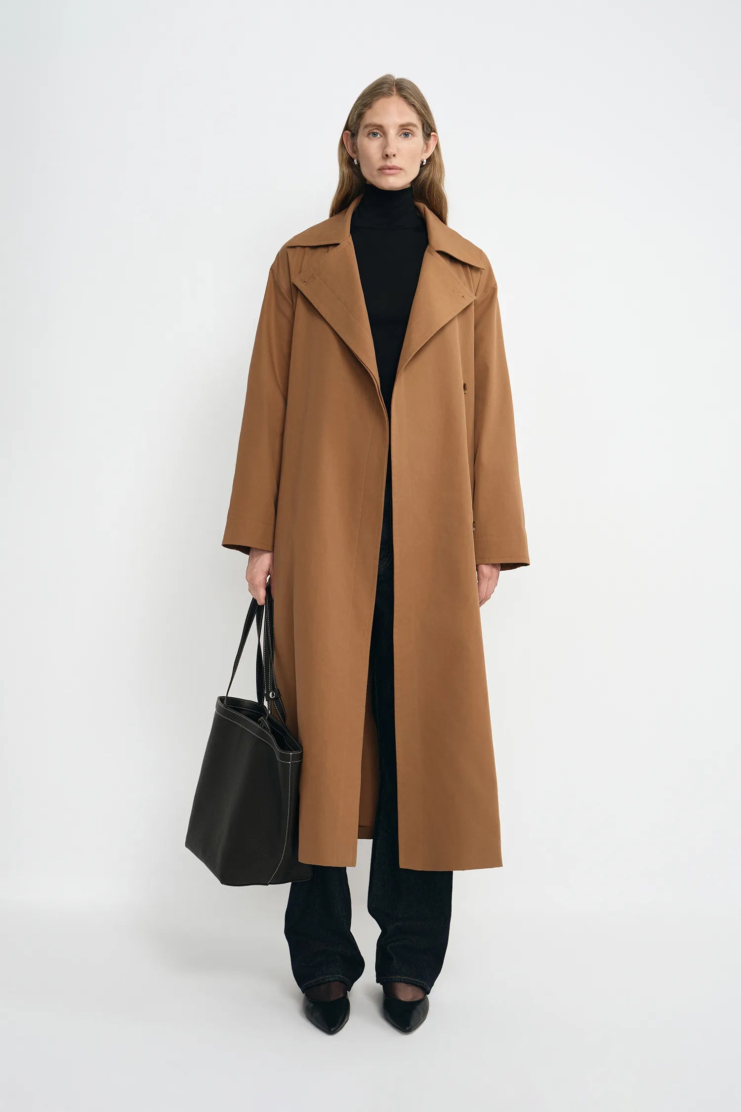 A model wearing a coppery brown oversized trench coat, open front, pairing dark wash jeans.