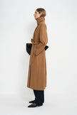 A model wearing a coppery brown oversized trench coat with a self-tie belt, side view.