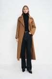 A model wearing a coppery brown oversized trench coat, pairing a black turtleneck and dark wash jeans.
