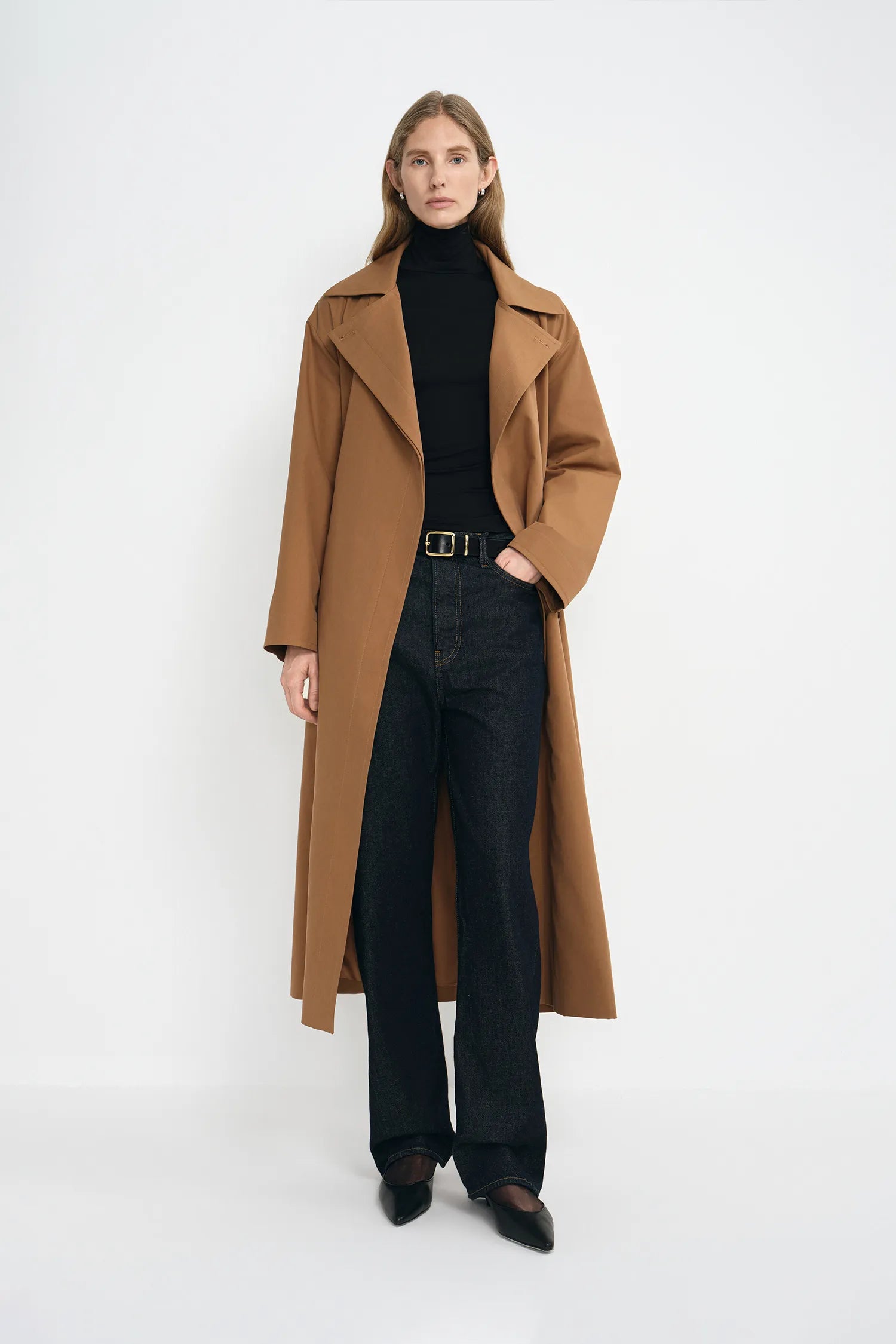 A model wearing a coppery brown oversized trench coat, pairing a black turtleneck and dark wash jeans.