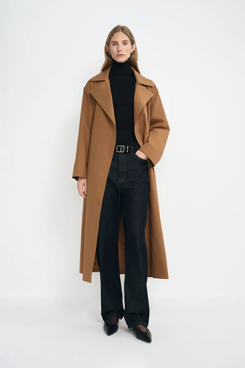 A model wearing a coppery brown oversized trench coat, pairing a black turtleneck and dark wash jeans.