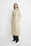 A model wearing an oatmeal oversized trench coat with a self-tie belt, pairing charcoal wide-leg trousers, facing the camera.
